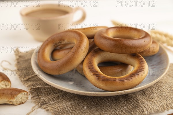 Homemade Ring Bagel with cup of coffee on white wooden background and linen textile. side view,