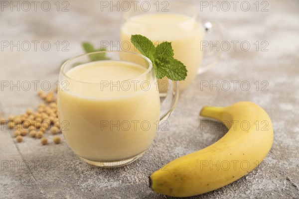 Organic non dairy banana and soy milk in glass on brown concrete background. Vegan healthy food