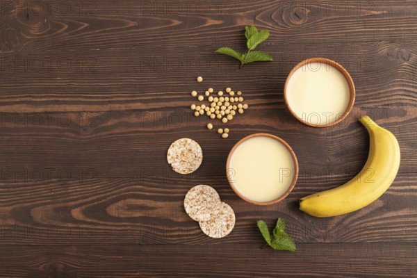 Organic non dairy banana and soy milk in clay cup on brown wooden background. Vegan healthy food