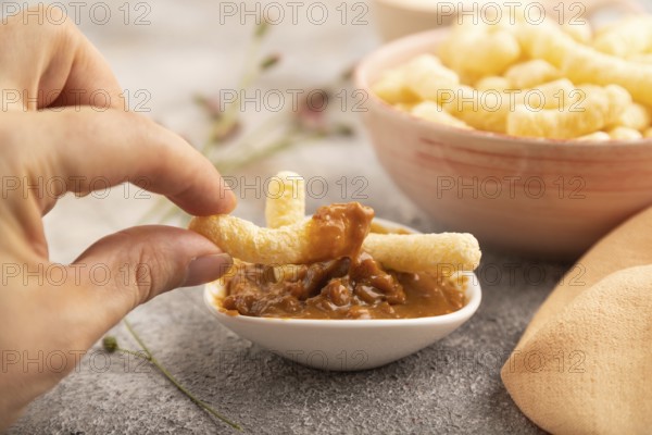 Corn flakes sticks with hand with caramel in ceramic bowl on gray concrete background and orange