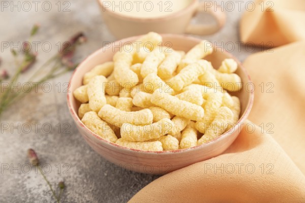 Corn flakes sticks with caramel in ceramic bowl on gray concrete background and orange linen