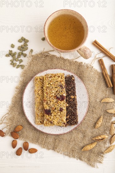 Granola bars with caramel, nuts, flakes in ceramic plate on white wooden background, beige linen