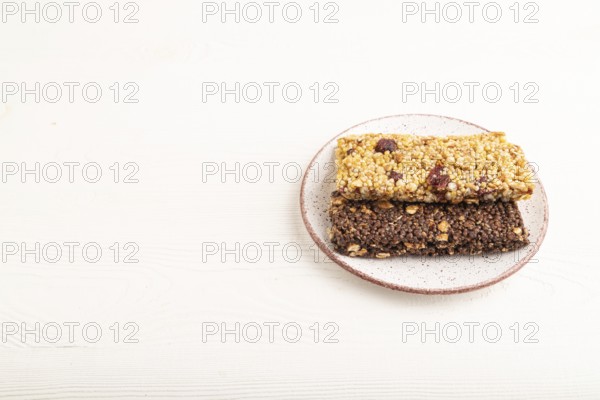 Granola bars with caramel, nuts, flakes in ceramic plate on white wooden background. Side view,