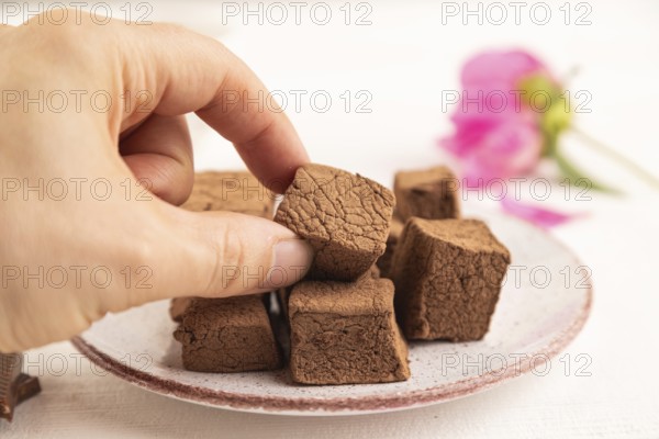 Chocolate marshmallow with cup of coffee with hand on white wooden background. side view, close up,