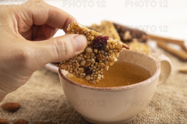 Granola bars with caramel, nuts, flakes in ceramic plate with hand on white wooden background,