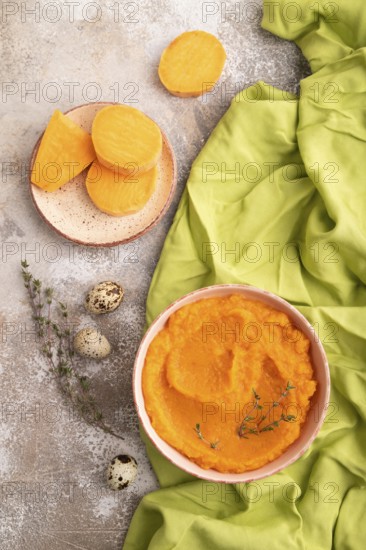 Sweet potato porridge in ceramic bowl on brown concrete background and green textile. Diet, healthy