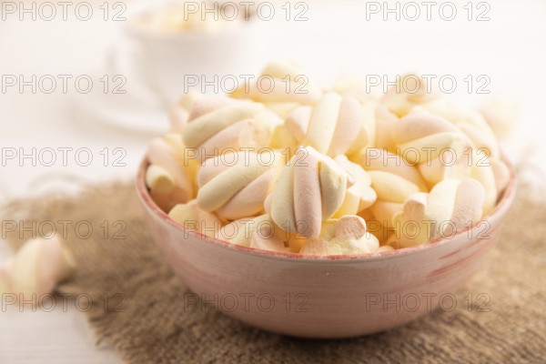Orange and pink marshmallow in ceramic bowl on white wooden background, side view, close up,