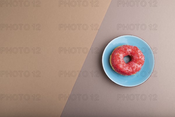 Pink Donut with sprinkles on blue ceramic plate on beige and gray pastel paper background, top