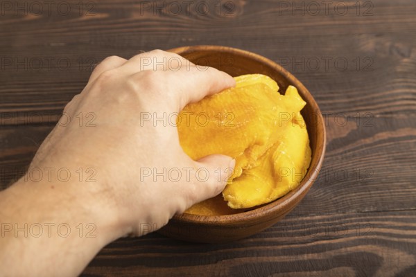 Dried Mango in wooden bowl with hand on brown wooden background. Side view, close up. healthy food,