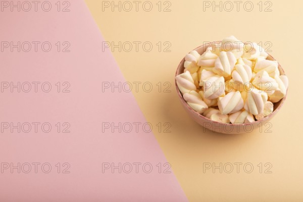 Orange and pink marshmallow in ceramic bowl on pink and orange pastel paper background, side view,