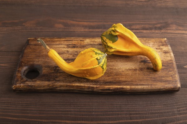 Two decorative orange Pumpkins on cutting board on brown wooden background, side view, close up,