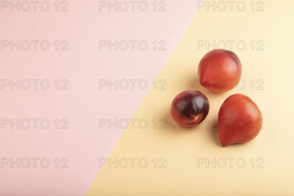 Red Heart shape tomatoes on pink and orange pastel paper background. Side view, copy space. healthy