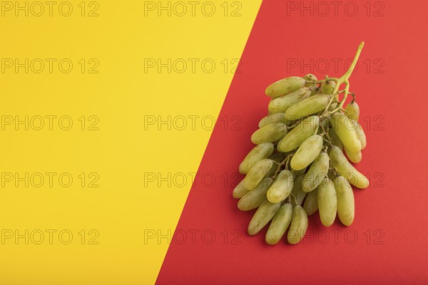 Green grapes on yellow and red paper pastel background. Side view, copy space. healthy food,