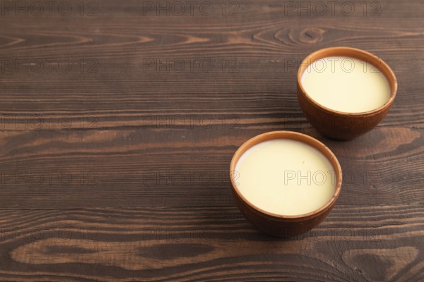 Organic non dairy banana and soy milk in clay cup on brown wooden background. Vegan healthy food