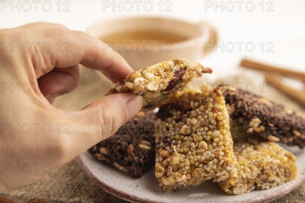 Granola bars with caramel, nuts, flakes in ceramic plate with hand on white wooden background,