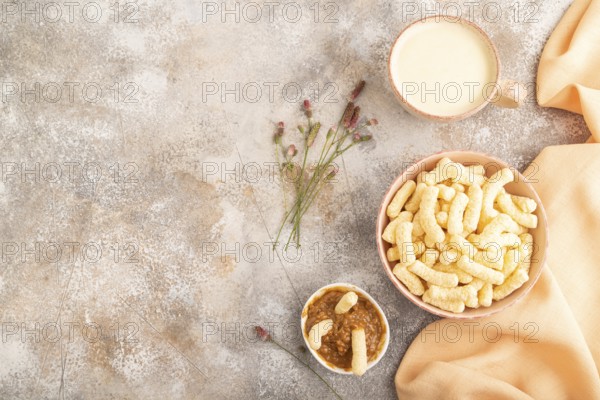 Corn flakes sticks with caramel in ceramic bowl on gray concrete background and orange linen
