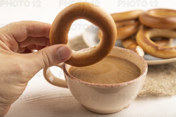 Homemade Ring Bagel with hand with cup of coffee on white wooden background and linen textile. side