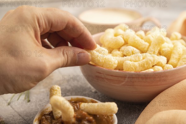 Corn flakes sticks with hand with caramel in ceramic bowl on gray concrete background and orange