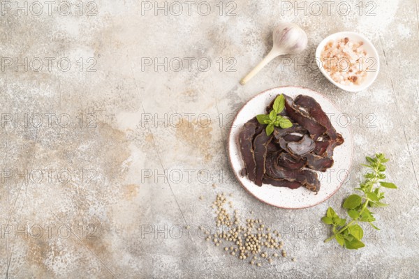 Armenian Basturma dried meat on plate with pepper and herbs on brown concrete background. Top view,