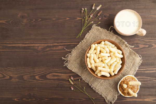Corn flakes sticks with caramel in wooden bowl on brown wooden background and linen textile. Top