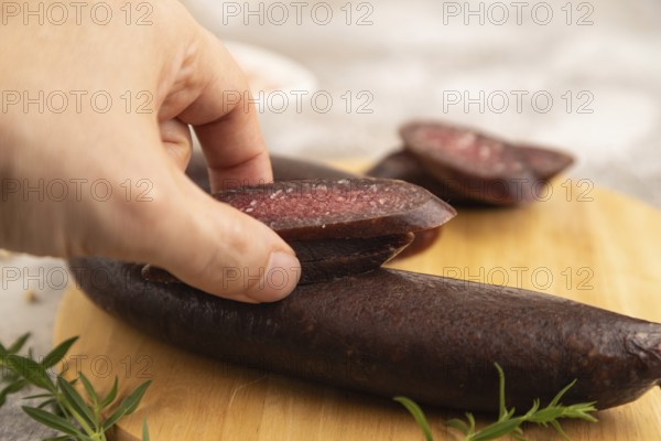 Sujuk sausage with hand on wooden cutting board with pepper and herbs on brown concrete background.
