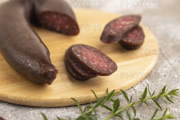 Sujuk sausage on wooden cutting board with pepper and herbs on brown concrete background. Side