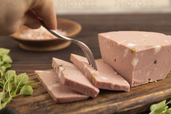 Mortadella sausage with hand on wooden cutting board with pepper and herbs on brown wooden