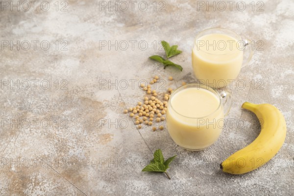 Organic non dairy banana and soy milk in glass on brown concrete background. Vegan healthy food
