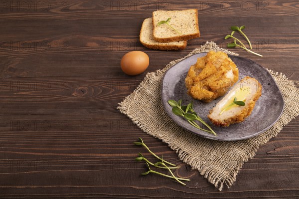 Chicken Schnitzel on gray plate with microgreen on brown wooden background and linen textile. side