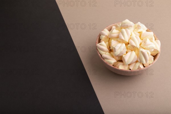 Orange and pink marshmallow in ceramic bowl on black and beige pastel paper background, side view,