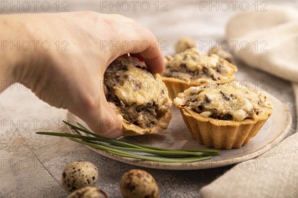 Tartlets with meat and cheese with hand on brown concrete background and linen textile. side view,