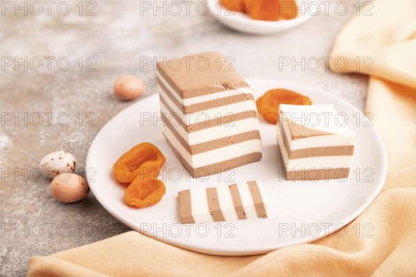 Cocoa and milk jelly with dried apricots on brown concrete background and orange textile, side