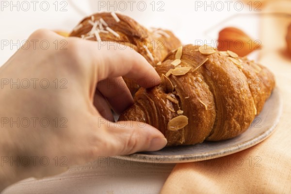 Croissant on blue plate with hand on white wooden background and orange linen textile, side view,