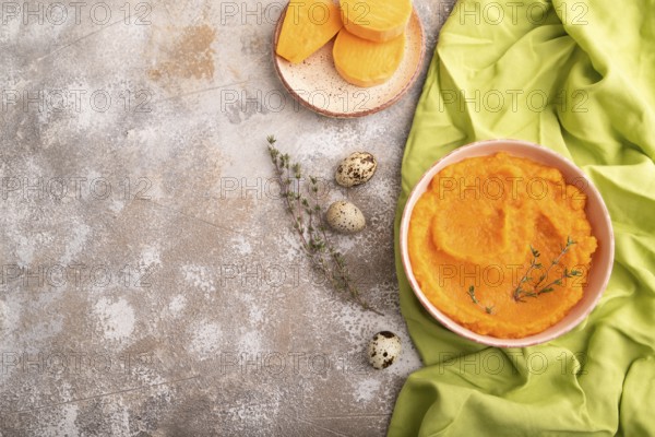 Sweet potato porridge in ceramic bowl on brown concrete background and green textile. Diet, healthy