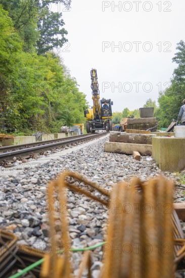 Baustelle mit Bahnschienen und Bagger in einer von Bäumen umgebenen Umgebung, sichtbar sind