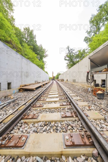Eisenbahngleise zwischen Betonwänden führen in die Ferne, umgeben von Wald, Bau der Hermann