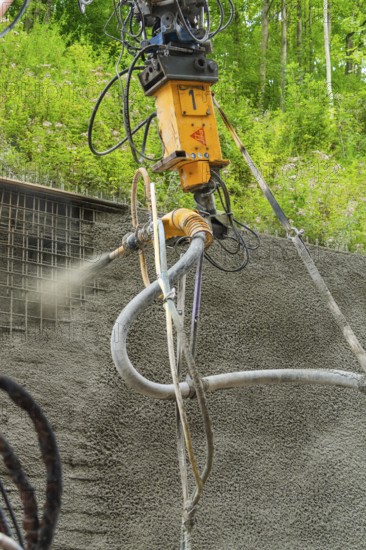 Nahaufnahme einer Maschine, die Beton auf eine Struktur sprüht, umgeben von grüner Vegetation, Bau
