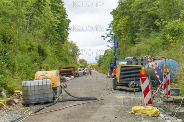 Baustellenszene mit Maschinen und Geräten entlang einer Straße in bewaldetem Gebiet, Bau der
