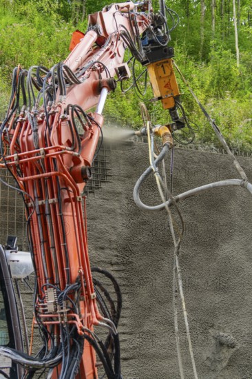 Industrielles Baugerät sprüht Beton auf strukturierten Untergrund umgeben von Vegetation, Bau der