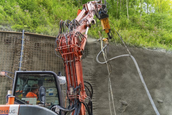 Maschine sprüht Beton an einer Wand entlang eines bewachsenen Bauplatzes, Bau der Hermann