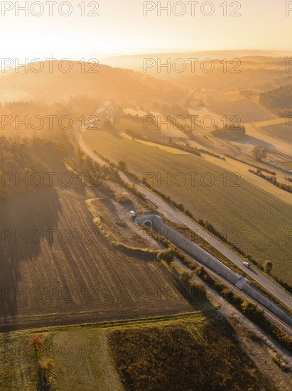 Landschaft während eines Sonnenaufgangs mit Feldern, Hügeln und einer Straße, die von goldenem