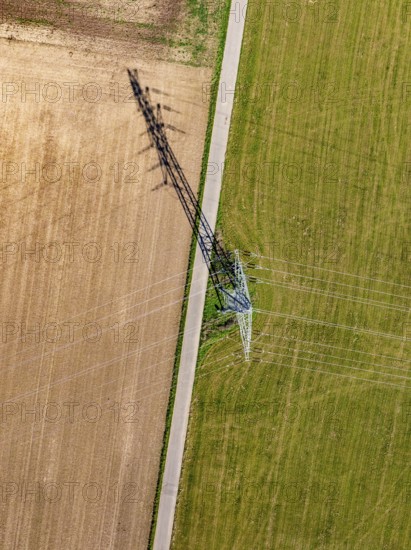 Strommast thront zwischen Acker und Wiese, mit einem langen Schatten der sich über das Feld