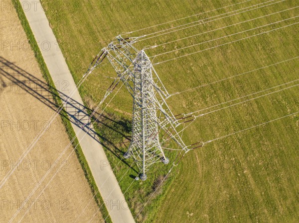Hochspannungsmast auf einer Wiese, mit langen Schatten, eingefangen aus der Vogelperspektive,