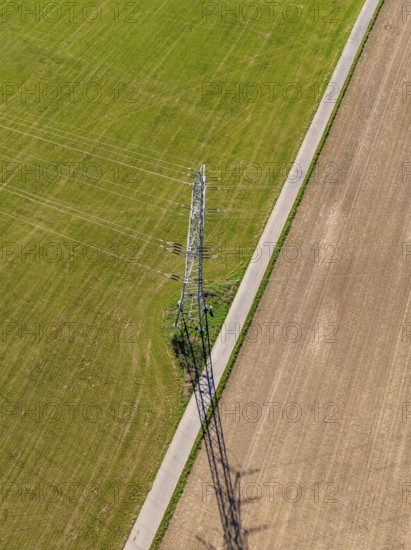 Luftbild eines Strommasts auf einer Wiese, umgeben von Feldwegen und langen Schatten, Nagold,