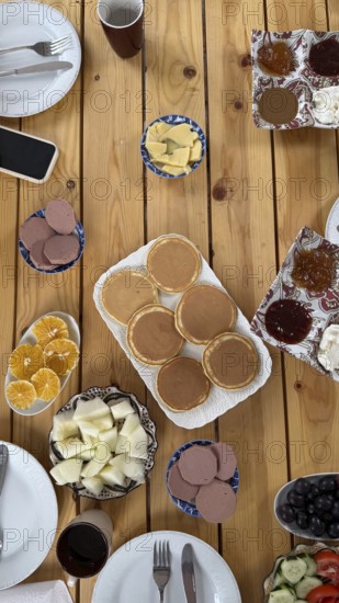 Wooden table spread of traditional moroccan breakfast, pancakes, sliced oranges and melon, olives,