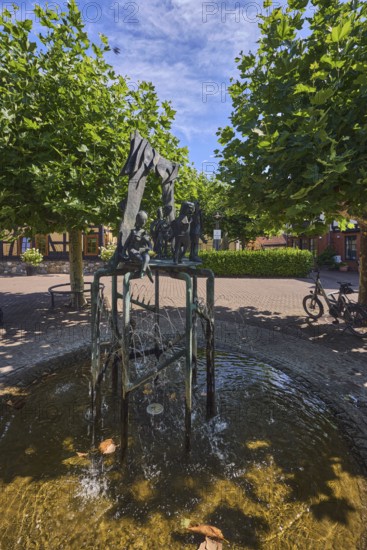 Brunnen mit Metallskulpturen, Alltägliches Theater, Bildhauer Hugo Uhl, Platz, Bäume, Hecke, blauer