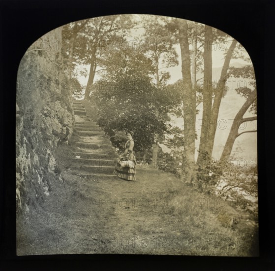Magic lantern slide of woman standing in countryside next to a flight of steps through woodland,