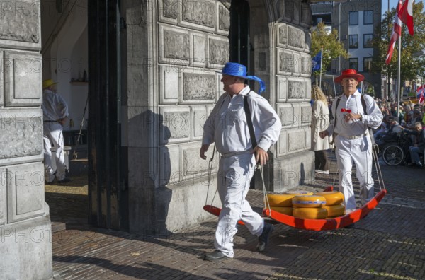 Men in traditional clothing transporting cheese at a historic building, cheese carrier, cheese,