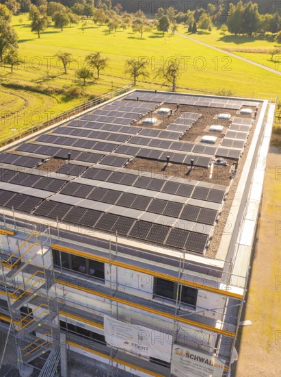Close-up of a building with solar panels and scaffolding in green surroundings, new building with