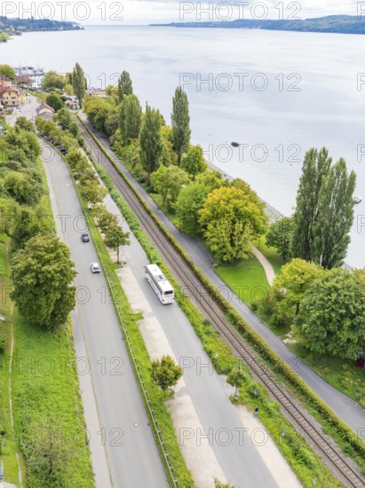 Aerial view of a road and railway line along a lake with trees and buildings, Lake Constance